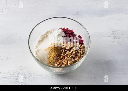 Recipiente di vetro con una miscela di farina, zucchero, spezie, noci e mirtilli rossi su sfondo azzurro. Cucinare deliziose torte fatte in casa. Foto Stock