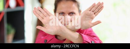 Donna con faccia seria mostra le braccia incrociate come simbolo di no, stop, negata e rifiutata. Foto Stock