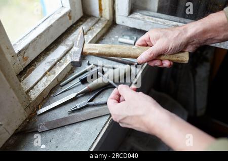 Mano degli uomini che tiene il martello. Riparazione del vecchio finestrino danneggiato o smontaggio prima dell'installazione di un nuovo, primo piano. Riparazione del telaio di un finestrino, mediante strumenti per Foto Stock