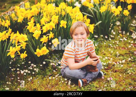 Simpatico bambino con coniglio pasquale al cioccolato per festeggiare la festa tradizionale. Famiglia, vacanza, primavera, concetto di infanzia spensierata. Foto Stock