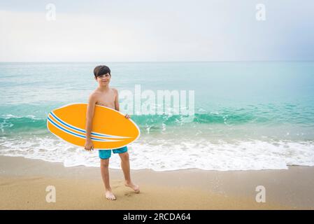 Ritratto di un ragazzo adolescente sorridente con tavola da surf gialla in piedi sulla spiaggia Foto Stock