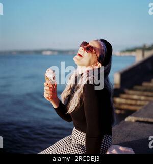 La donna con i capelli viola assaggia il gelato su un molo di Alki Beach Foto Stock