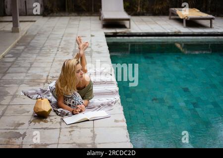 Una giovane donna passa del tempo vicino alla piscina, scrivendo un diario. Foto Stock