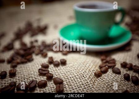 Messa a fuoco selettiva sui chicchi di caffè sulla iuta con una tazza verde sullo sfondo Foto Stock