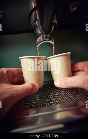 mani maschili caucasiche che tengono due tazze di carta sotto il getto di caffè nero Foto Stock