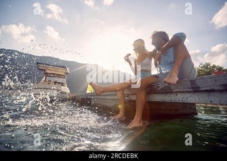 Giovane uomo e donna innamorati flirtando e godendosi le gambe penzolanti nel lago Foto Stock