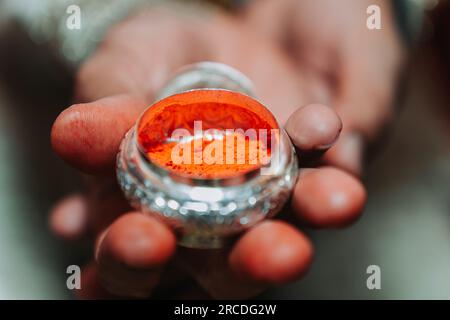 La mano di The Groom che tiene sindur o Vermiglio prima di applicare sulla separazione dei capelli della sposa.fuoco selettivo Foto Stock