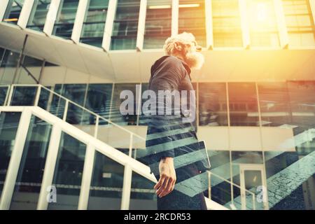 Uomo d'affari anziano con barba cammina davanti a un ufficio moderno Foto Stock