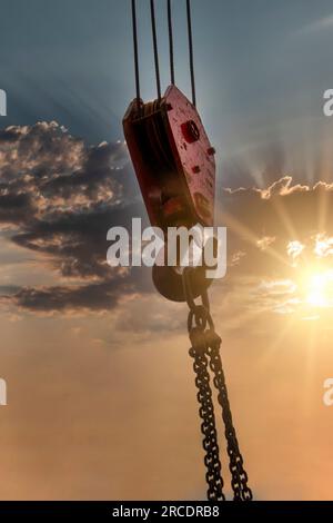 gancio gru con pesi di sollevamento a catena al tramonto Foto Stock