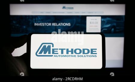 Persona che tiene il cellulare con il logo della società statunitense Methode Electronics Inc. Sullo schermo di fronte alla pagina Web aziendale. Concentrarsi sul display del telefono. Foto Stock