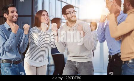 Gruppo di manager felici gioire di un accordo di successo stringendo le mani in pugni e sollevandoli Foto Stock