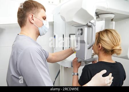 Giovane donna fare riprese panoramiche della ganascia tenendo il suo volto alla macchina a raggi x Foto Stock