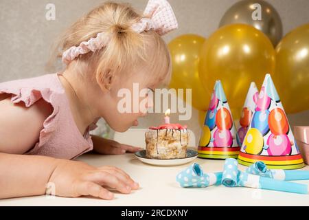 Una bambina di due anni fa spara una candela su una torta di compleanno, fa un desiderio Foto Stock