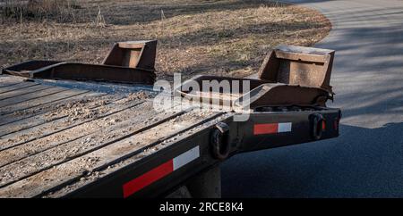 Rampe rialzate sul retro di un rimorchio a pianale vuoto parcheggiato sulla strada asfaltata, al sole nel tardo pomeriggio. Foto Stock