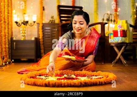 Felice ragazza indiana tradizionale che decora Rangoli con fiori per la celebrazione del festival diwali al piano a casa - concetto di cultura, costumi e Foto Stock