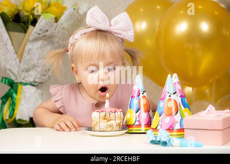 Una bambina di due anni fa spara una candela su una torta di compleanno, fa un desiderio Foto Stock