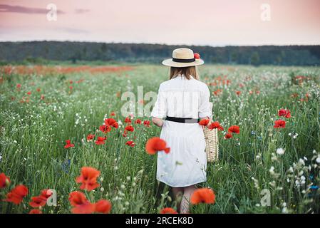 Bella ragazza con papaveri e grano. ritratto all'aperto. Bambino in abito bianco che raccoglie papaveri e fiordaliso nel campo estivo. Simbolo di memoria papaveri in fiore. Ragazza del villaggio. Foto Stock