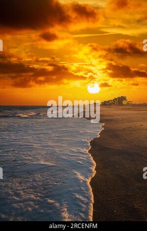 Onde di bianco schiuma di mare lavarsi su una spiaggia alla luce della sera. Foto Stock