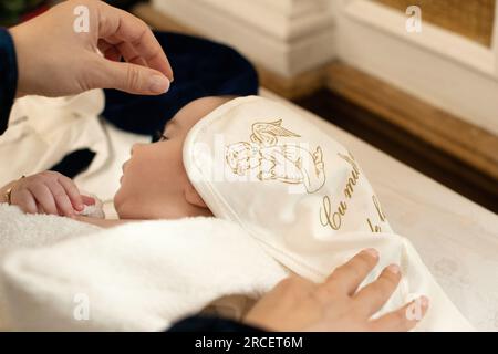 La madrina avvolge il bambino in un asciugamano dopo il battesimo in chiesa Foto Stock