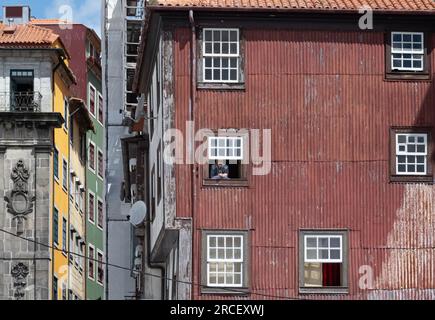 Porto, Portogallo - 25 aprile 2023: Uomo che fuma nella finestra di un vecchio edificio rosso fatiscente sul fiume Douro a Porto, in Portogallo Foto Stock