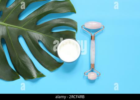 Rullo massaggiante per il viso con due testine al quarzo rosa. Massaggio di bellezza facciale, trattamento spa self-care. Rullo massaggiante e crema viso su una foglia monstera Foto Stock