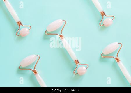 Rulli per massaggio facciale in quarzo rosa su sfondo blu posizionati fianco a fianco. Massaggiatore facciale antirughe e anti-invecchiamento, strumento per la cura della pelle Foto Stock