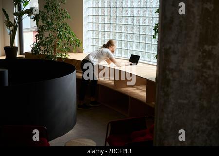 Un giovane maschio con un computer portatile si trova vicino a un rack di legno Foto Stock