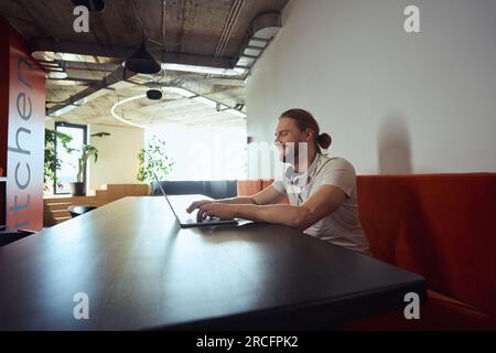 Happy maschio con computer portatile nella zona cucina dello spazio di coworking Foto Stock