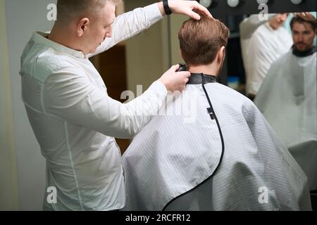 Barbiere esperto che utilizza il regolacapelli elettrico in un moderno salone Foto Stock