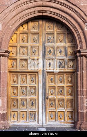 Grande porta in legno decorata, incorniciata da un arco in pietra decorato. Ingresso a iglesia de nuestra senora de guadalupe, Teguise, Lanzarote, Canarie ISL Foto Stock