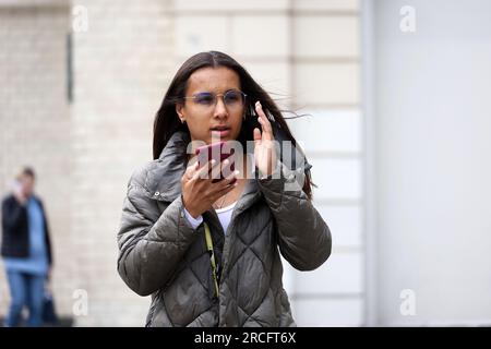 Ragazza con gli occhiali che parla sullo smartphone utilizzando il vivavoce mentre cammina per strada. Uso del telefono cellulare nelle città estive Foto Stock