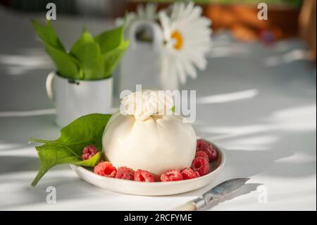 burrata con frutti di bosco e un coltello da formaggio sul tavolo della cucina al sole. Copia spazio Foto Stock