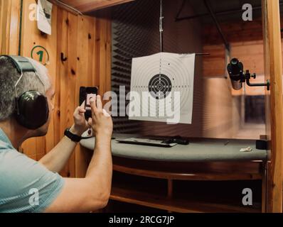 Un uomo in un poligono scatta una foto ed esamina i risultati dopo la ripresa Foto Stock