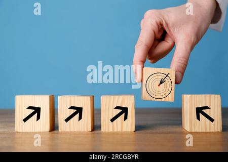 Donna che mette un cubo con l'icona del bersaglio in una fila di cubi con frecce su sfondo azzurro, primo piano Foto Stock