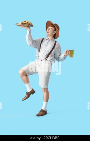 Giovane in abiti tradizionali tedeschi con birra e spuntini che ballano su sfondo blu Foto Stock