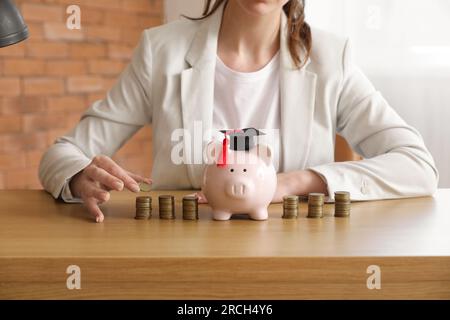 Donna in abito da lavoro seduta al tavolo con salvadanaio e pile di monete. Concetto di prestito studentesco Foto Stock