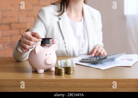 Donna in abito da lavoro seduta al tavolo con pile di monete, banconote in dollari e salvadanaio. Concetto di prestito studentesco Foto Stock