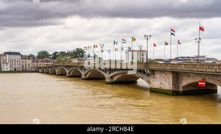 Grande ponte con bandiere di vari paesi che attraversa il fiume della città di Bayonne in Francia. Foto Stock