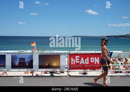 Un uomo in pantaloncini da surf e un cappello di cotone passeggia davanti alla mostra fotografica del 2022 Head on sul lungomare di Bondi Beach, Foto Stock