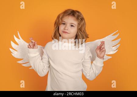 L'angelo bambino incrociò le dita con fortuna e speranza, Buona fortuna. San Valentino. Piccolo angelo bambino cupido con le ali. Studio ritratto di bambino angelico. Foto Stock