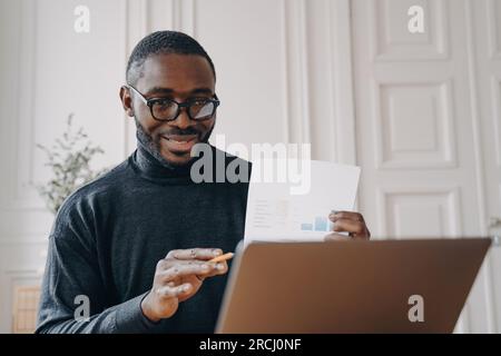 Il freelance afroamericano indossa occhiali ha una videoconferenza remota, tiene un rapporto finanziario durante una riunione online. Foto Stock