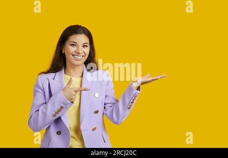 La bella donna sorridente punta il dito sullo spazio di copia isolato su sfondo giallo brillante. Foto Stock