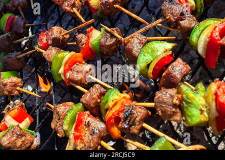 barbecue all'aperto, piccole fiamme su spiedini di legno di kebab con peperoni di carne rossa e cipolle Foto Stock