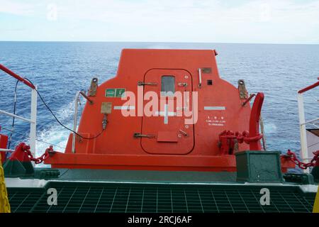 Poppa di una scialuppa di salvataggio a caduta libera arancione con porta fissata sulla rampa di lancio e pronta per lanciare e abbandonare la nave. Foto Stock