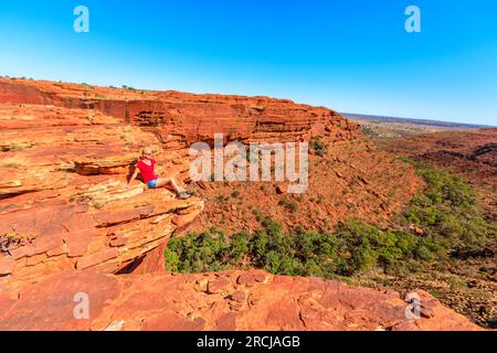 Ragazza turistica seduta ai margini del Kings Canyon nel Parco Nazionale di Watarrka, il Red Center australiano. Trekking del Rim Walk vicino al bordo del canyon. Nord Foto Stock