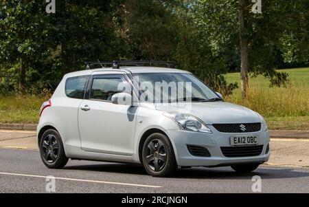 Milton Keynes, Regno Unito - 13 luglio 2023: 2012 auto bianca SUZUKI SWIFT che guida su una strada inglese. Foto Stock