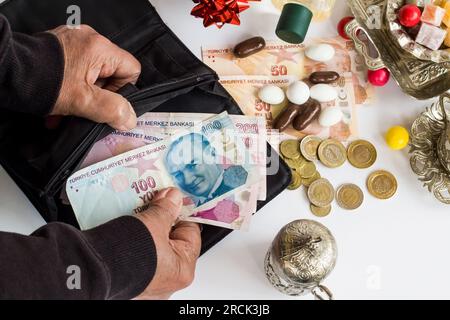 Old Hand prende la lira turca dal portafoglio nero su una superficie bianca con caramelle colorate e set da caffè turco. Bonus festa riflesso nel design delle pensioni Foto Stock