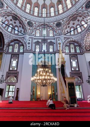 Due uomini siedono e discutono come un altro prega all'interno della moschea Yeni valida a Uskudar, Istanbul, Turchia Foto Stock