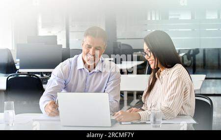Manager maturo latino maschio e giovane lavoratrice asiatica che guarda il laptop. Foto Stock