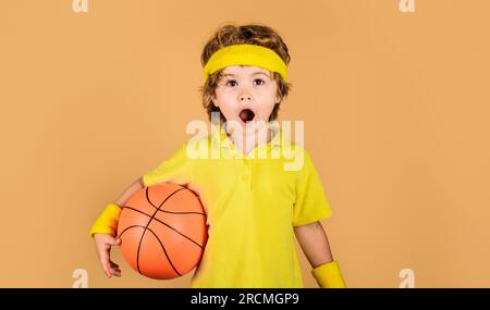 Stile di vita sportivo attivo, infanzia. Sessione di allenamento di basket per bambini. Ragazzo sorpreso con la palla da basket. Piccolo pallacanestro in abbigliamento sportivo. Sport Foto Stock